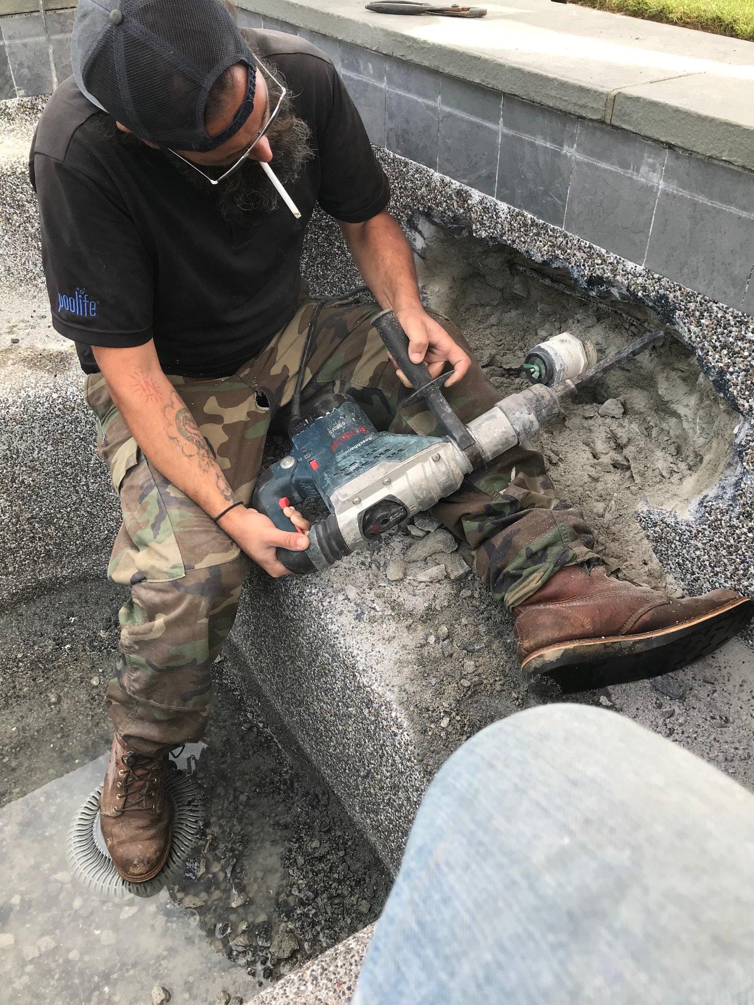 Technician jackhammering pool deck concrete to access underground plumbing for leak repair