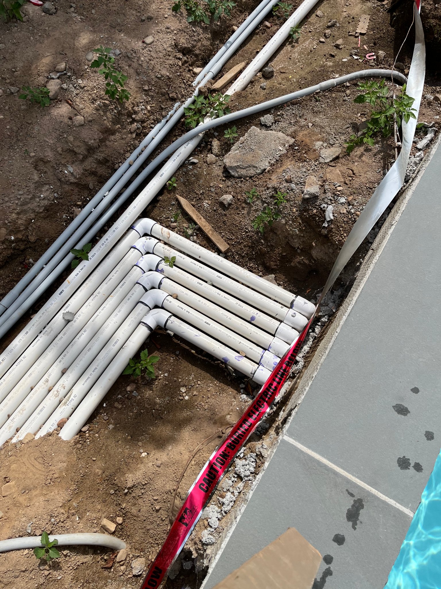 New PVC pool plumbing manifold installed alongside pool deck during repair
