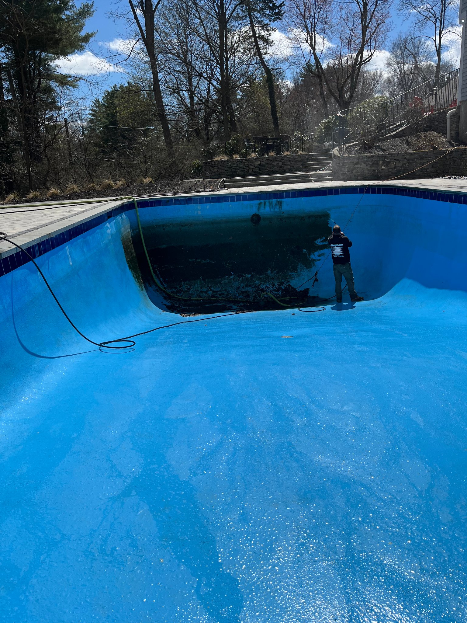 Technician pressure washing pool walls during spring opening service